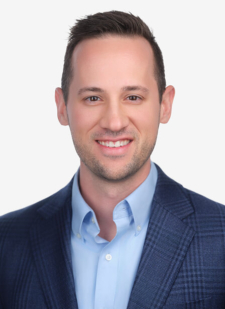 A smiling man with short dark hair, wearing a blue suit jacket and light blue shirt, against a plain white background.