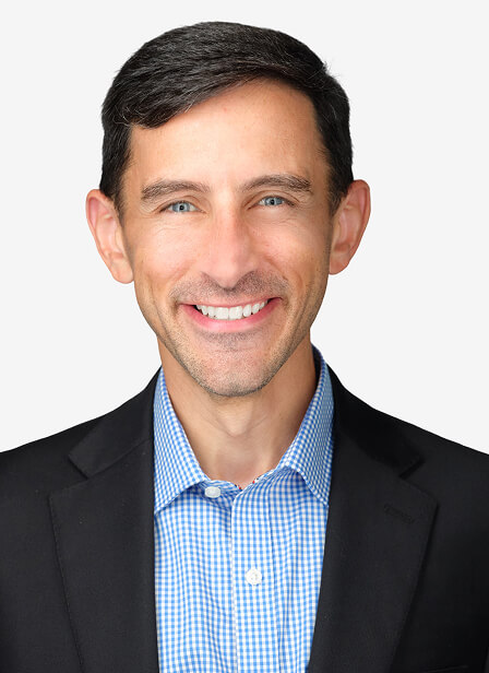 Andrew Henson, smiling man in a suit and blue checkered shirt, poses against a plain white background.