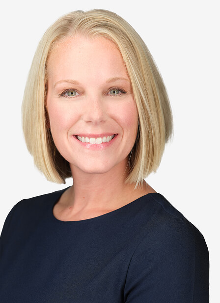 A smiling woman with shoulder-length blonde hair wearing a dark navy top against a plain white background.