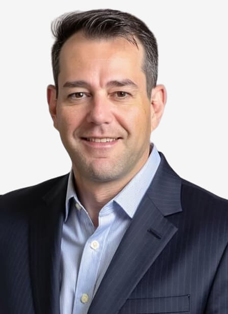 A professional man with short dark hair, wearing a dark pinstripe suit and light blue shirt, smiling confidently against a