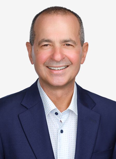 A smiling middle-aged man with short hair, wearing a navy blazer and white shirt, against a plain light background.