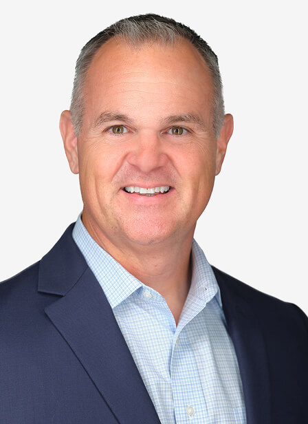 A smiling man in a navy blazer and light blue shirt poses against a plain background.