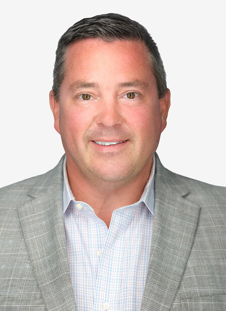 A man with short dark hair, wearing a light gray checkered blazer and a light blue shirt, smiling confidently.