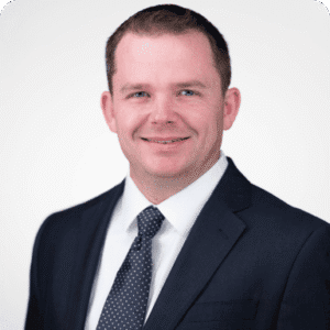 Jason Marchant, dressed in a dark suit and tie, smiles confidently against a plain light background.